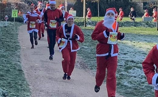 A group of runners dressed in Santa suits with white beards and red hats participating in a festive race.