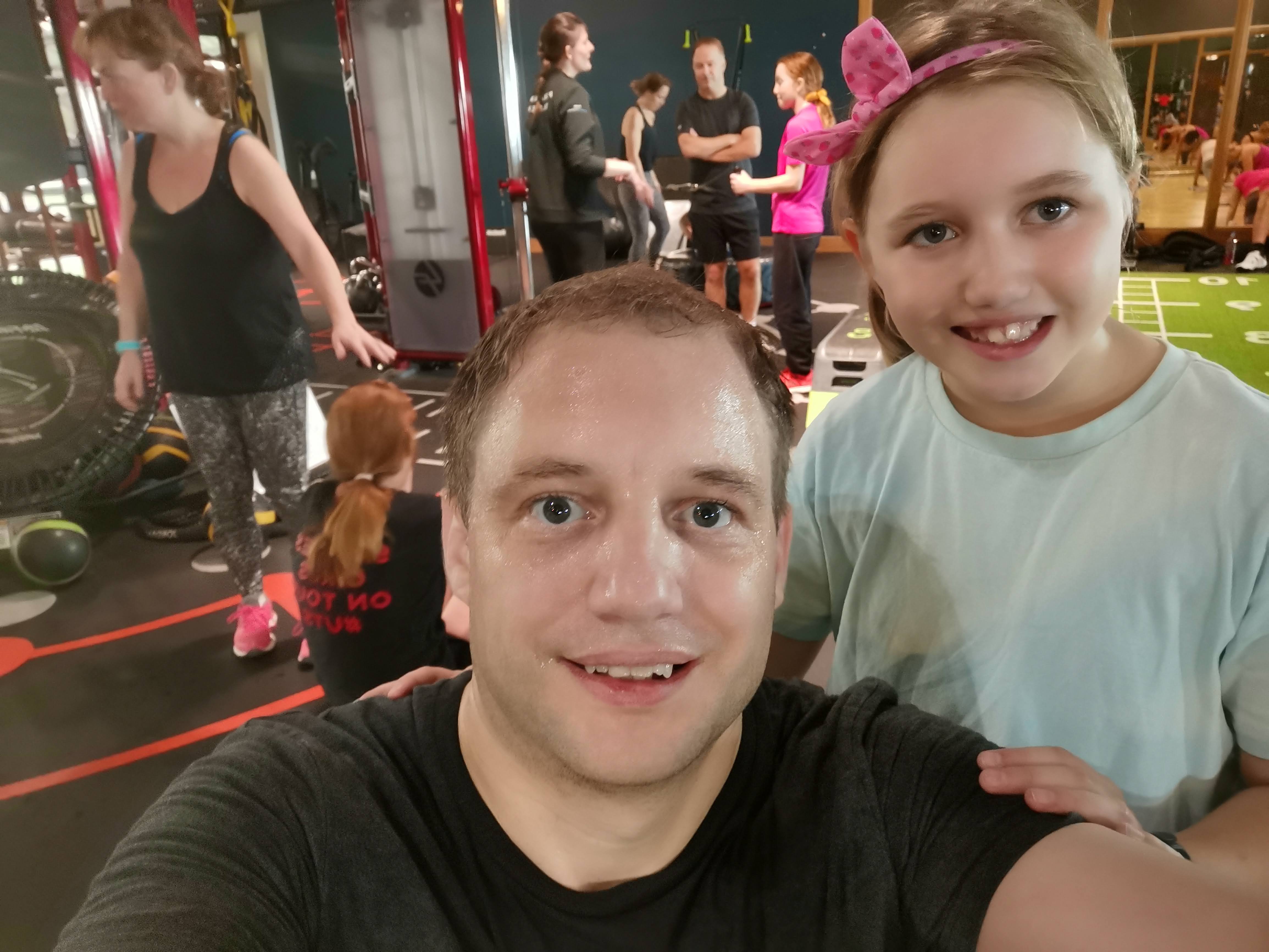 Myself and Hanna taking a smiling selfie in the gym, both looking at the camera, with other people exercising in the background